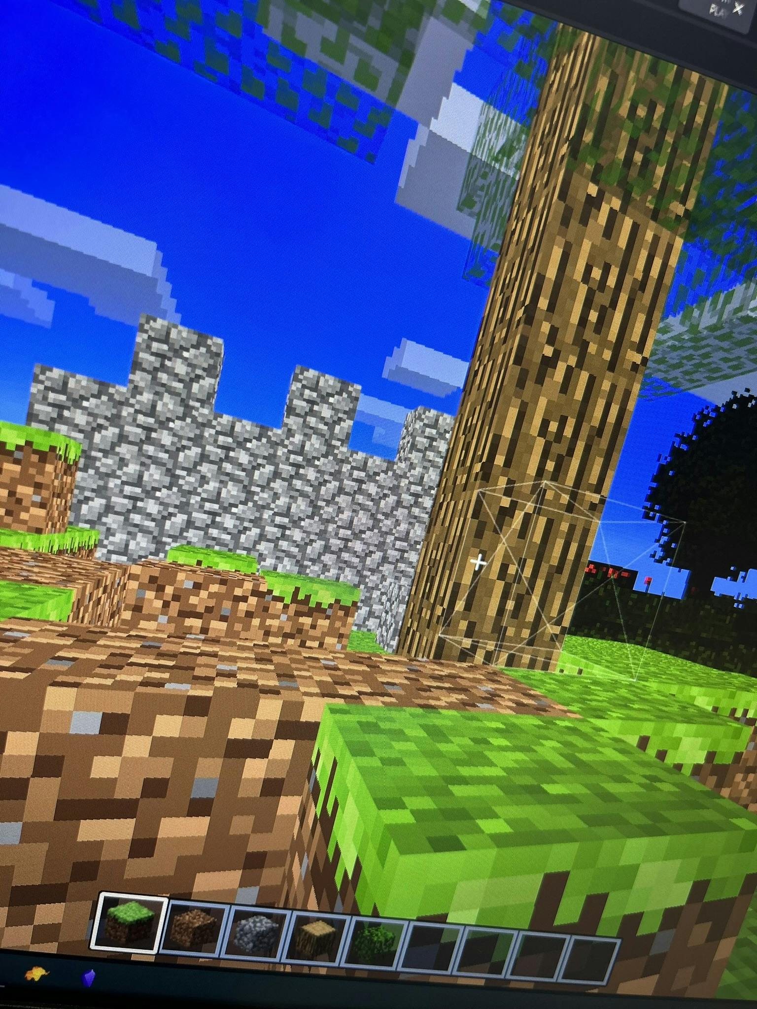 A Minecraft-like sandbox game. There's a block selector at the bottom which includes a grass, dirt, cobblestone, wood and leaves block. In front, there are grass and leaves block placed in the terrain.